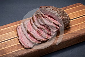 Sliced Grass Fed juicy Corn Roast Beef on wood cutting board.