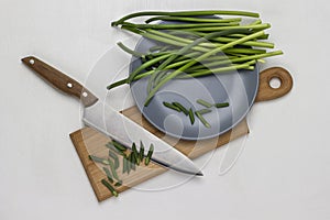 Sliced green shoots of garlic and a knife on a cutting board. Shoots of garlic on a gray plate