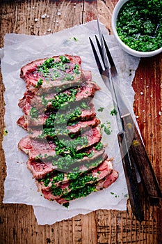 Sliced grilled barbecue beef steak with green chimichurri sauce