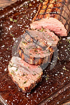 Sliced grilled beef tenderloin seasoned with salt, rosemary and thyme on a wooden cutting board