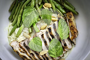 Sliced grilled chicken and string bean with peanuts and mint leaves on noodle in a white bowl. Top view.