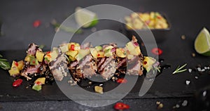 Sliced grilled fried tuna steak covered with sesame seeds and mango salsa on a black stone serving board