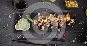 Sliced grilled fried tuna steak covered with sesame seeds and mango salsa on a black stone serving board