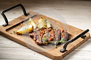 Sliced grilled meat steak Ribeye medium rare serving on wooden serving board with potatoes on table.