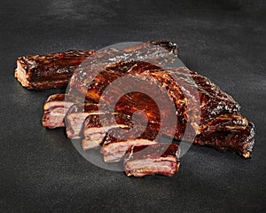 Sliced grilled pork ribs in barbecue sauce on stone surface