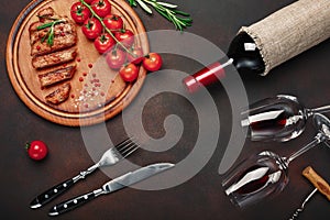 Sliced grilled pork steaks with bottle of wine, wine glass, corkscrew, knife, fork, black bread, cherry tomatoes and rosemary on