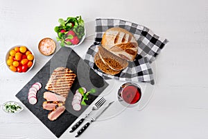 Sliced grilled roast beef with fork and knife on stone serving board.