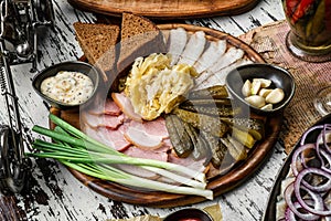 Sliced ham, bacon, lard, pickles, green onions, slices of rye bread on cutting board over rustic background. Appetizer for vodka,