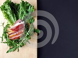 Sliced ham with fresh green lettuce leaves on a cutting board.