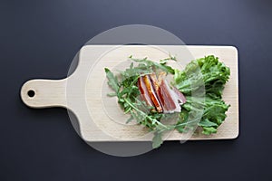 Sliced ham with fresh green lettuce leaves on a cutting board.