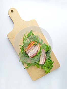 Sliced ham with fresh green lettuce leaves on a cutting board.