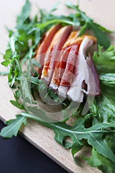 Sliced ham with fresh green lettuce leaves on a cutting board.