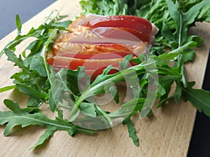 Sliced ham with fresh green lettuce leaves on a cutting board.