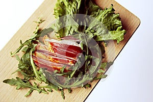 Sliced ham with fresh green lettuce leaves on a cutting board.