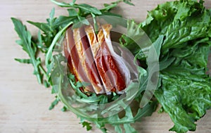 Sliced ham with fresh green lettuce leaves on a cutting board.