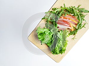 Sliced ham with fresh green lettuce leaves on a cutting board.