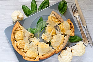 Sliced healthy cauliflower pie on the gray plate decorated with fresh basil leaves and vintage silver knife and fork