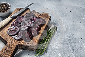 Sliced Horse dried sausage on woooden board with herbs. Gray background. Top view. Copy space