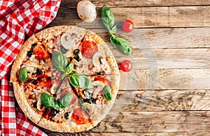 Sliced italian pizza with salami, mozzarella, mushroom, tomatoes, black olives and basil leaves on black background. Italian