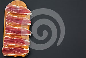 Sliced jamon Serrano or Iberico on cutting wooden board. Traditional spanish hamon on dark wooden background, top view.