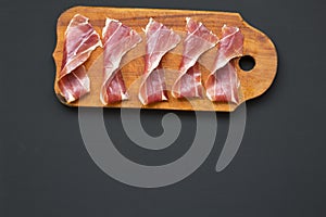 Sliced jamon Serrano or Iberico on cutting wooden board. Traditional spanish hamon on dark wooden background, top view. Copy