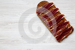 Sliced jamon Serrano or Iberico on cutting wooden board. Traditional spanish hamon on white wooden background, top view.