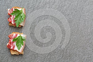 Sliced jerky with greens on cereal bread. Dark background.