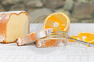 Sliced lemon cake with a fork and some fresh orange fruit slices