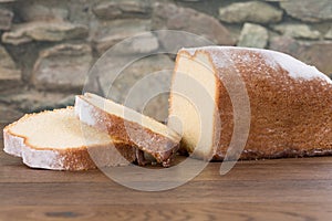 Sliced lemon cake on a wooden table with a stone wall