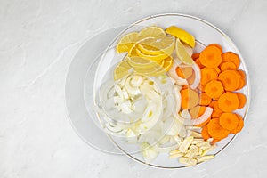 Sliced lemons, onions, garlic and carot on the plate ready for cooking