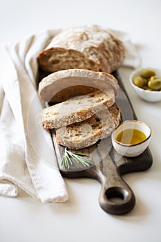 Sliced loaf of bread on a cutting board. Olive oil, olives and basil