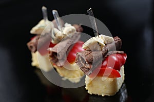 Sliced meat, rolled into a roll, canapes with blue cheese and red pepper, on a skewer, close-up