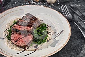 Sliced medium rare grilled beef steak with mushroom sauce and greens on a plate on wooden background