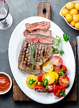 Sliced medium rare grilled beef steak served on white plate with tomato salad and potatoes balls. Barbecue, bbq meat