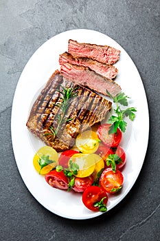 Sliced medium rare grilled beef steak served on white plate with tomato salad and potatoes balls. Barbecue, bbq meat