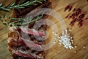 Sliced medium rare grilled steak on rustic cutting board with rosemary and spices , dark rustic metal background, top