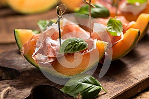 Sliced melon with ham and basil leaves, served on a wood chopping board