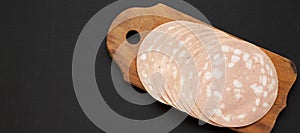 Sliced Mortadella Bologna Meat on a rustic wooden board over black background, top view. Flat lay, from above, overhead. Space for