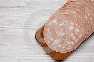 Sliced Mortadella Bologna Meat on a rustic wooden board over white wooden background, view from above. Flat lay, top view,