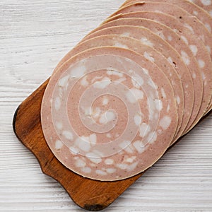 Sliced Mortadella Bologna Meat on a rustic wooden board over white wooden surface, top view. Flat lay, from above, overhead. Close