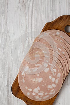 Sliced Mortadella Bologna Meat on a rustic wooden board over white wooden surface, view from above. Flat lay, top view, overhead.