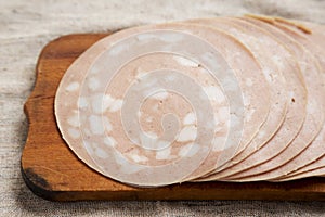 Sliced Mortadella Bologna Meat on a rustic wooden board, side view. Close-up