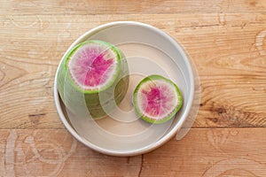 Sliced open watermelon radish in a white bowl on an old wooden table