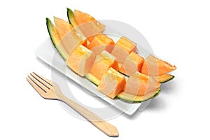 Sliced orange melon in pieces on a white plate with wooden fork.