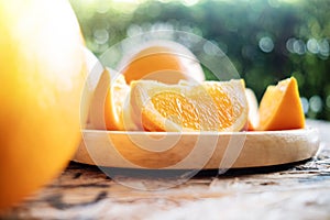 Sliced Orange on Wooden Plate. Fresh Juicy Fruit in Summer. Selective Focus. Blurred Tree with Lens Flare