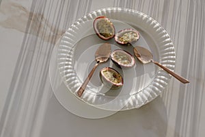 Sliced passion fruits served on a white plate with copper spoons.