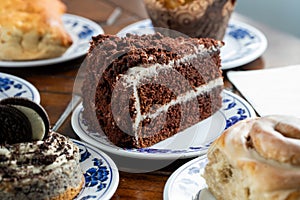 Sliced piece  of a delicious chocolate cake on a blue-white plate surrounded with other sweets