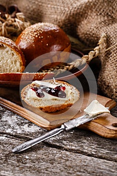 Sliced piece of freshly baked buns with butter and jam on wooden kitchen board.