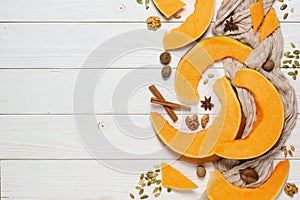 Sliced pieces of pumpkin  with seeds, nuts, cinnamon sticks, and spices on a white wooden background