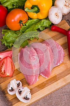 Sliced pieces of raw meat for barbecue with fresh Vegetables tomatoes, lettuce on wooden surface. Top view.